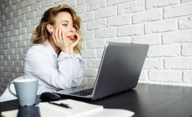 Kıvırcık saçlı bir kadın laptopuyla masada oturuyor..