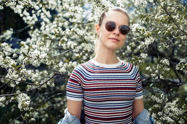 Ung kvinna i solglasögon på bakgrunden av blommande äppelträd — Stockfoto