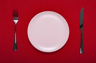 beyaz boş tabak çatal ve bıçak üzerinde kırmızı bir masa örtüsü