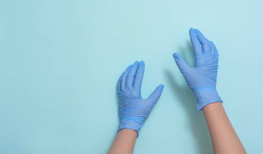 Mavi arka planda elleri tıbbi eldivenlerle yakın plan.