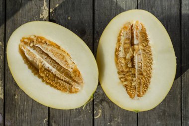 Ahşap kesme tahtasının üzerinde kavun ikiye bölünmüş. Üst görünüm.