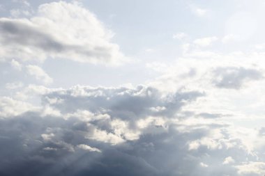 Dramatik kara bulutlu gökyüzü, beyaz ve gri kümülüs bulutları mavi gökyüzünde hareket ediyor ve güneş ışınları yükseliyor, doğa arka planı