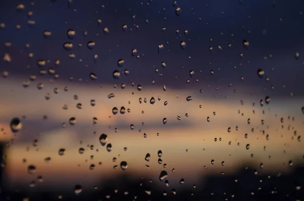 Pluie fenêtre extérieure sur fond de coucher de soleil. La pluie tombe sur le verre pendant la pluie. Texture lumineuse des gouttes d'eau — Photo