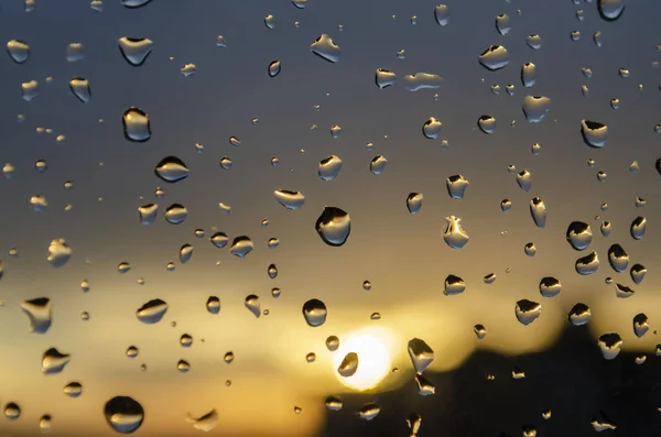 Pluie fenêtre extérieure sur fond de coucher de soleil. La pluie tombe sur le verre pendant la pluie. Texture lumineuse des gouttes d'eau — Photo