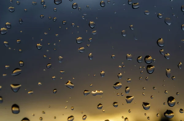 Pluie fenêtre extérieure sur fond de coucher de soleil. La pluie tombe sur le verre pendant la pluie. Texture lumineuse des gouttes d'eau — Photo