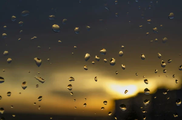 Rain outside window on background of sunset. Rain drops on glass during rain. Bright texture of water drops