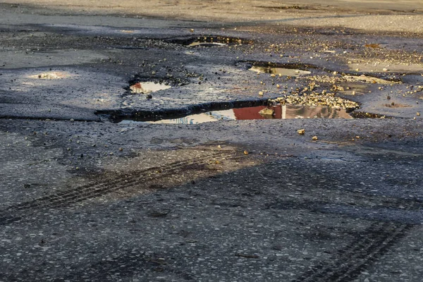 Gropar på vägen. Närbild fotografi av en del av vägen, asfalt som det finns många gropar där regnvatten hälls — Stockfoto