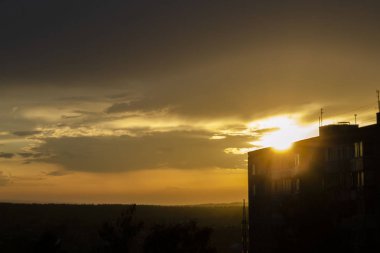 Şehir binalarının arkasında parlak turuncu güneş batıyor.