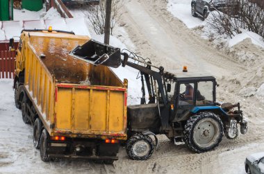 Traktör karları şehirden çıkarmak için kamyona yüklüyor.