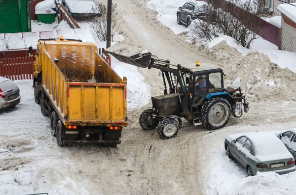 tractor loads the snow in the truck for snow removal from the city