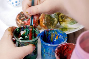 Çocuk, Paskalya için yumurta boyamak için boyaya bir fırça batırıyor.