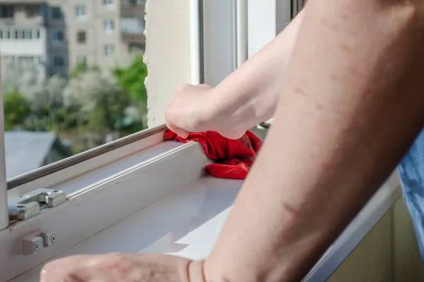 Woman washes a window and window sill with a red rag