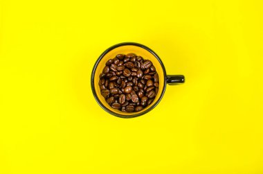 Siyah kenarlı bir fincan ve içinde sarı kahve taneleri olan sarı bir arka plan.