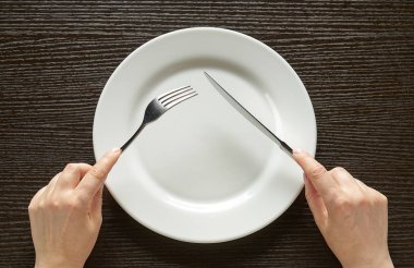 Fork and knife in hands on wooden background with white plate