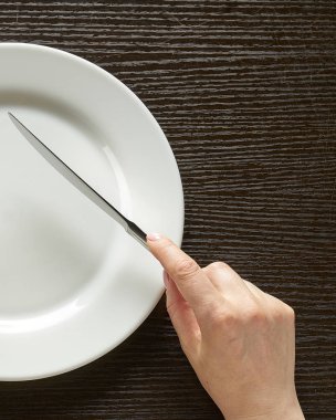 Fork and knife in hands on wooden background with white plate