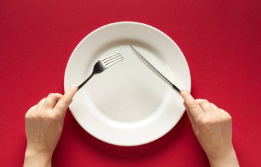 Fork and knife in hands on red background with white plate