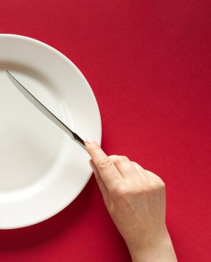 Fork and knife in hands on red background with white plate