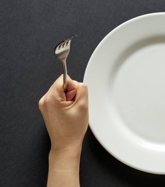 Fork and knife in hands on black background with white plate