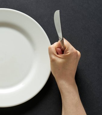 Fork and knife in hands on black background with white plate