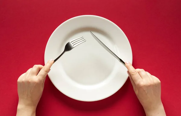 Fork and knife in hands on red background with white plate — 图库照片