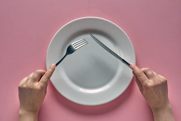 Fork and knife in hands on rose background with white plate — 图库照片