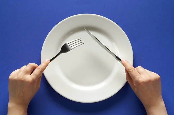Fork and knife in hands on cobalt color background with white plate — 图库照片