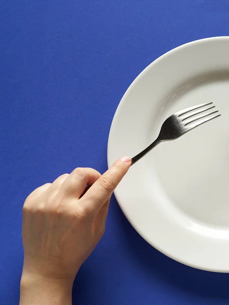 Tenedor y cuchillo en las manos sobre fondo de color cobalto con placa blanca — Foto de Stock
