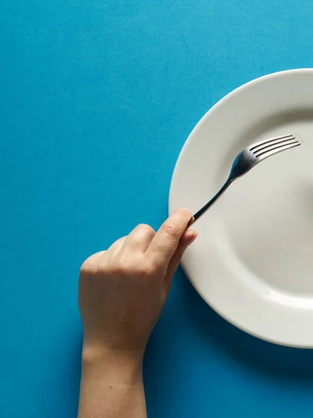 Fork and knife in hands on blue color background with white plate — 图库照片