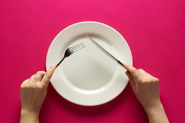 Fork and knife in hands on red background with white plate — Stockfoto