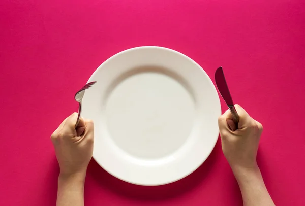 Tenedor y cuchillo en las manos sobre fondo rojo con plato blanco —  Fotos de Stock