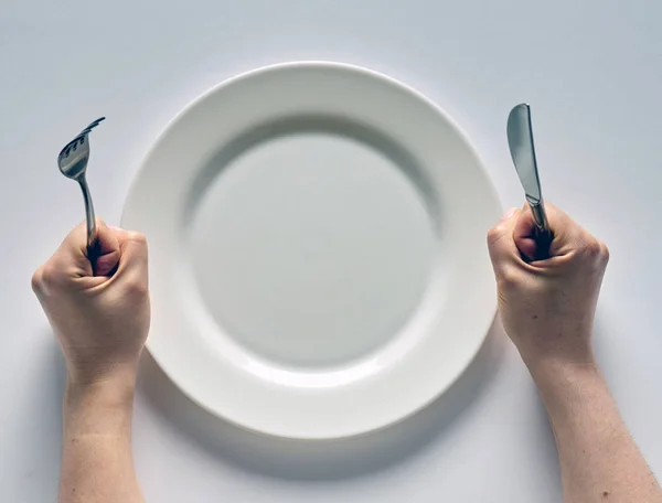 Fork and knife in hands on white background with white plate — Stockfoto