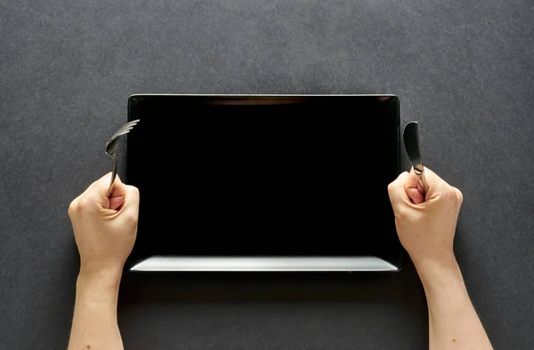 Fork and knife in hands on black background with black rectangular plate — 스톡 사진