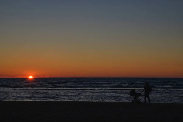 Silhouettes of young group of people jumping in ocean at sunset — Stock Photo, Image