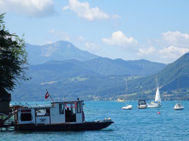 Gölün mavi sularındaki gemi, dağların arka planına karşı.
