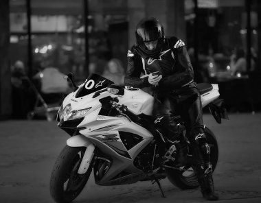 10-07-2018 Riga, Letonya. Motosikletli, siyah takım elbiseli, motosikletli, telefondaki mesajları okuyor. Motosikletli siyah beyaz