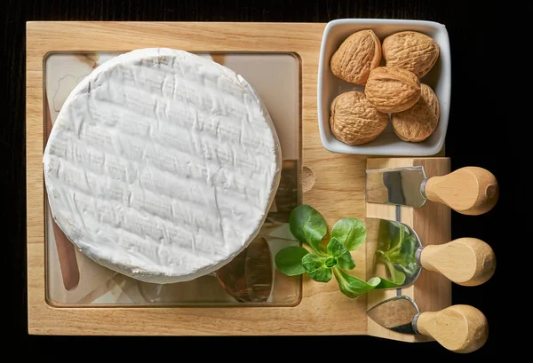 Camambertový sýr s ořechy a bazalkou na dřevěné řezací desce — Stock fotografie