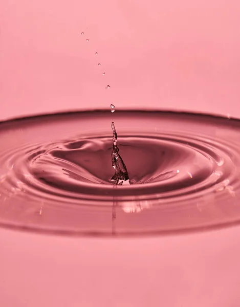 Wassertropfenspritzer in einem rosafarbenen Glas — Stockfoto