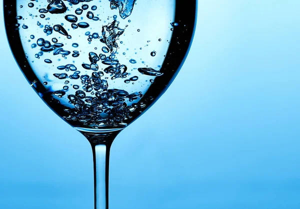 Pouring water into a glass against light blue background — 스톡 사진