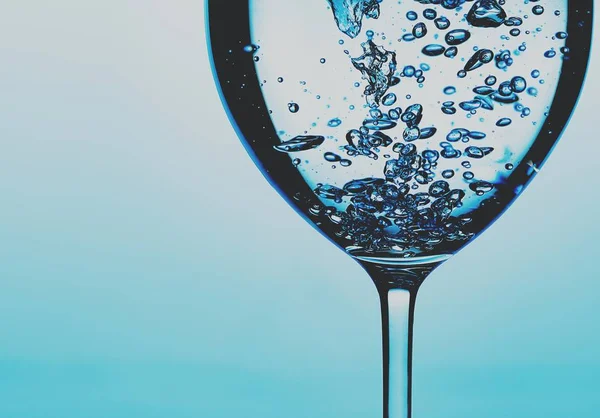Pouring water into a glass against light blue background — 스톡 사진