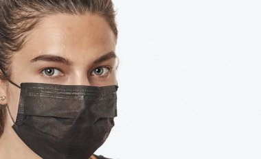 Steteskoplu, beyaz bir arka planda cerrahi maske takan güzel bir kadının yakın plan portresi..