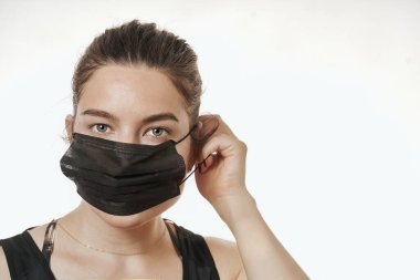 Beyaz bir arka planda, cerrahi maske takan güzel bir kadının yakın plan portresi.