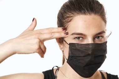 Yüzüne koruyucu maske takan genç bir kadın. Parmak tabancası gösteriliyor. Kendine güvenen kız, tıbbi maskeli kadın doktor ve koruyucu eldivenler. Coronavirus COVID-19 koruması