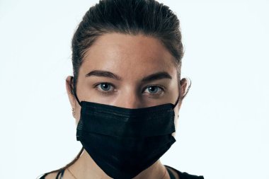 Beyaz bir arka planda, cerrahi maske takan güzel bir kadının yakın plan portresi..