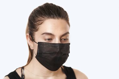 Beyaz bir arka planda, cerrahi maske takan güzel bir kadının yakın plan portresi.