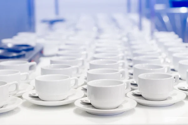 Many white coffee cups in a line over a buffet