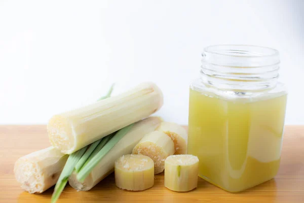 Temiz bardakta taze sıkılmış şeker kamışı suyu ve beyaz arka planda kesilmiş kamış..