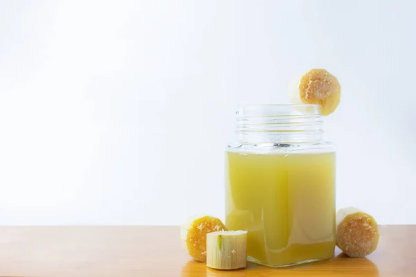 Temiz bardakta taze sıkılmış şeker kamışı suyu ve beyaz arka planda kesilmiş kamış..