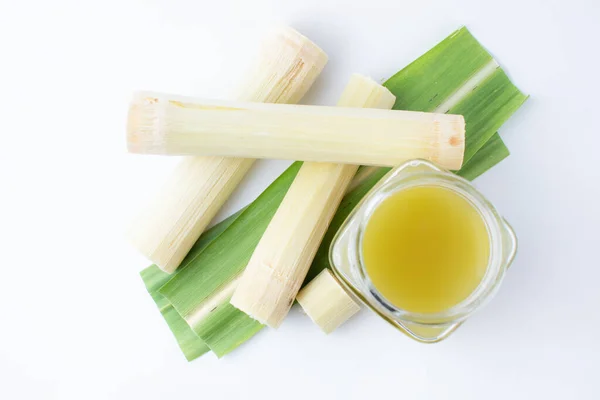 Temiz bardakta taze sıkılmış şeker kamışı suyu ve beyaz arka planda kesilmiş kamış..