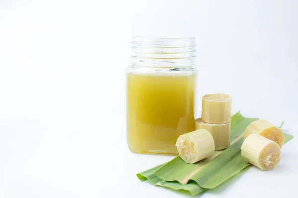 Temiz bardakta taze sıkılmış şeker kamışı suyu ve beyaz arka planda kesilmiş kamış..