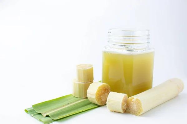 Temiz bardakta taze sıkılmış şeker kamışı suyu ve beyaz arka planda kesilmiş kamış..